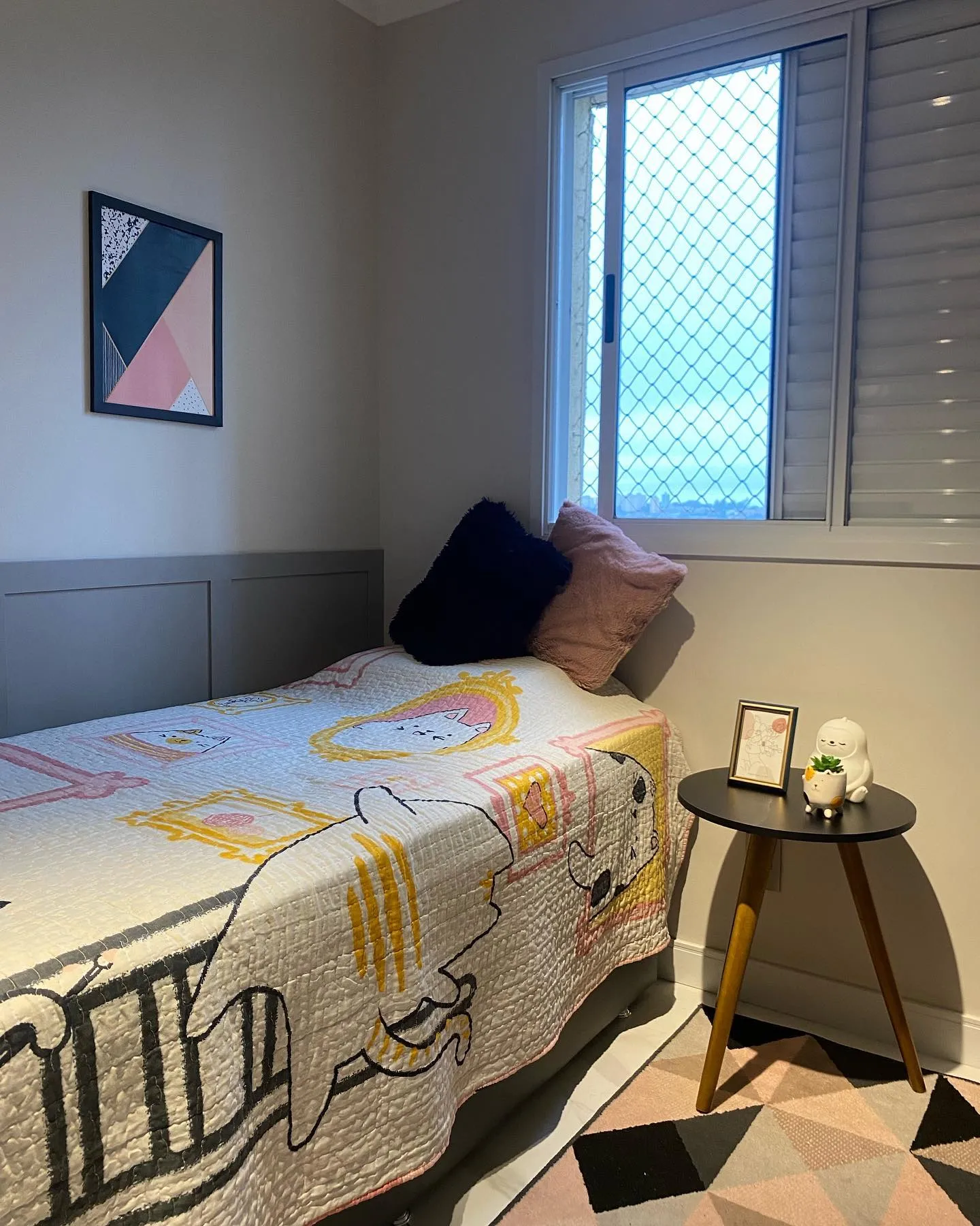 Dormitório juvenil com cama encostada na janela e roupa de cama estampada