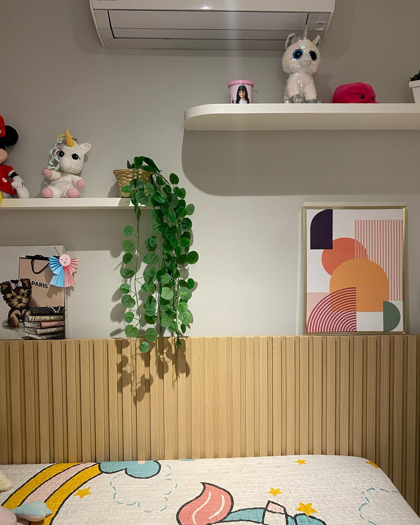 Quarto da Lari: cabeceira ripada de madeira, roupa de cama de unicórnios e prateleiras com pelúcias